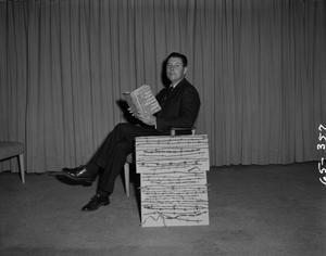Primary view of object titled '[Wane Brown sitting on chair with book]'.