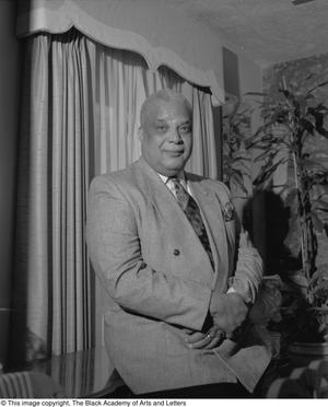 Black and white photograph of Claude McCain Jr. leaning on a desk.