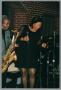 Primary view of [Photograph of Benita Arterberry holding a microphone next to a man playing a saxophone]