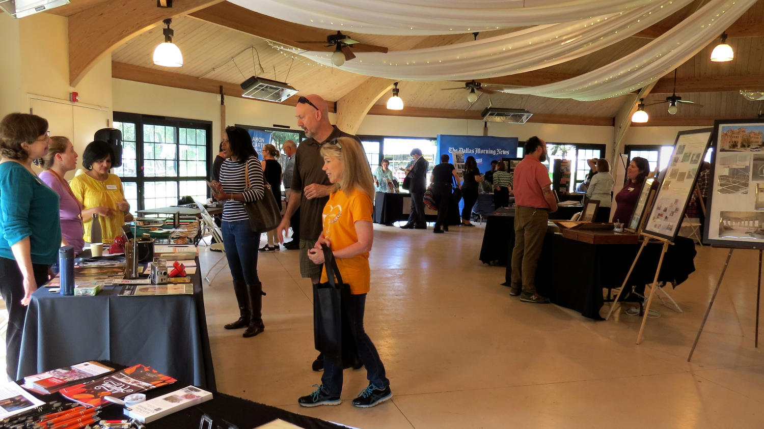 [Visitors walking up to the Sixth Floor Museum table], Photograph of visitors walking up to the Sixth Floor Museum at Dealy Plaza table during the DFW Archives Bazaar at the Dallas Heritage Village Pavilion. There are artifacts from the 60s including a small radio, a View-Master toy, copies of LIFE Magazine, a purse, a phone, and paper handouts., 
