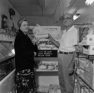 Primary view of object titled '[Man and woman holding donuts in front of store display 1 of 2]'.
