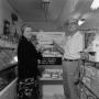 Photograph: [Man and woman holding donuts in front of store display 2 of 2]