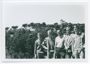 Foto en blanco y negro de 5 hombres de pie uno al lado del otro, una extensión de árboles detrás de ellos.