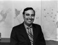 Photograph: [Ron Godbey in front of weather maps]