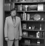 Photograph: [Broyles standing next to a bookcase]