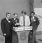 Photograph: [Four men standing behind a podium]