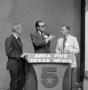 Photograph: [Three guests standing behind a podium]