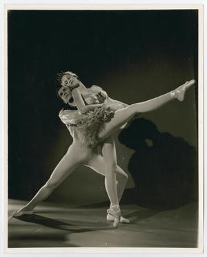 Dos bailarines de ballet, un hombre y una mujer. El hombre está de pie con las piernas separadas y la bailarina de ballet con una pierna en el aire.