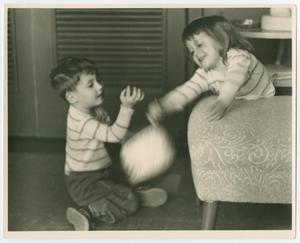 A young boy and a young girl play together. The girl is on the right on a couch, and the boy is on the floor in front of her.
