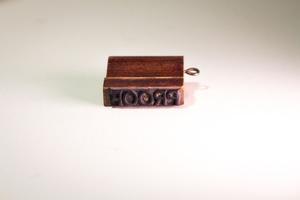 A small stamp shaped like a book, a wooden brown with the word Proof on the stamp part.