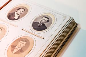 Closeup of a photo album page showing four small oval shaped photographs of men.