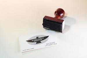 A shiny wooden stamper, and a white card next to it with the words Byrd Photo Service on it in a black eagle graphic.