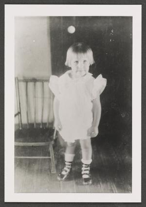 Primary view of object titled '[Photograph of a little girl standing next to a chair]'.