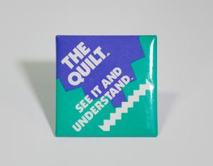 A square-shaped button, aqua and dark blue in color. The top left says  The Quilt, the middle says See It And Understand, under it a white squiggly line. The letters are diagonal.