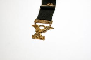 Black lanyard with a gold eagle pendant. Under its feet is the word Eagles, and above it the word Football.
