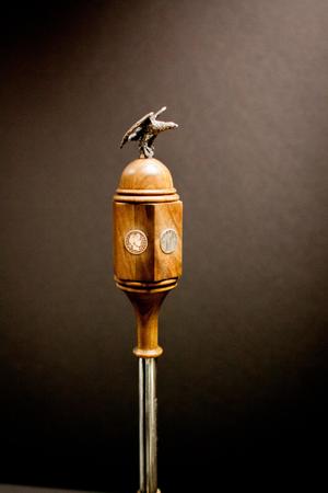 A wooden mace, with quarters on each side of the base. An eagle figurine is attached to the top, silver in color.