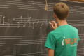 Photograph: [Student writing out score on chalkboard]