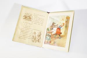 A book with a movable illustration on the right page that is pulled by a tab at the bottom. The illustration is of Little Red Riding Hood arching away from the brown wolf standing in front of her in her grandma's bonnet. The page on the left contains the story with a small sketch of a wolf at the top left corner, and another sketch on the bottom right.