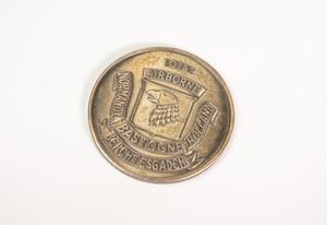 A rusted silver coin with an eagle head engraved in the middle, and the word Airborne at the top, and other lettering pertaining to the coin under it inside a ribbon.