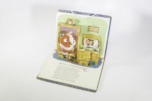 A pop-up of a book. The pop-up is of Santa Claus standing in a doorway on  the left with his gift bag on his back. On the right Rudolph is sleeping  peacefully in his bed. A sign above it reads Home Deer Home. Under the  pop-up the page has some text.