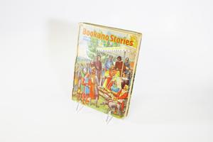A book cover of an illustration of a medieval scene, where a king sits down under a tent with his knight, and other servants by him and the tent surrounded by commoners. They are all outdoors.