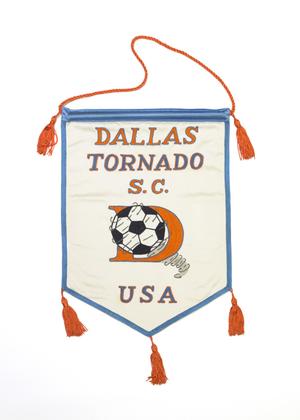 A white flag, outline by a light blue color and tied together by orange tassels. The top of the white banner says Dallas Tornado, and USA at the bottom. The middle of it is an orange letter D with a soccer ball on it.