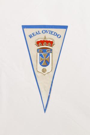 Una bandera triangular blanca, perfilada por un color azul claro. La parte superior lleva el título Real Oviedo en letras azules. Debajo hay una corona roja y una cruz.