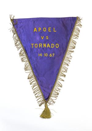 Una bandera púrpura flanqueada por hilo dorado, con las palabras APOEL vs Tornado en letras doradas, con la fecha debajo.