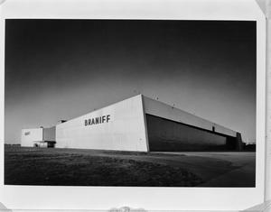 Black and white photo of a low, wide building, taken from a corner. The front of the building has a solid white front with the sign BRANIFF on one side.