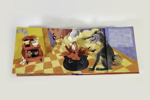 Photograph of an open pop-up book.The pages show a kitchen with a stove-pipe over, with gingerbread men popping out of the door. In the center of the pages is a large black cauldron with little red riding hood inside, her head, arms and feet stick out. The wolf sits to the right of the cauldron with a big grin and shakes pepper onto the girl.