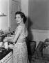 Photograph: [Photograph of Doris Stiles Williams standing in front of a stove]
