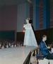 Photograph: [Woman in a dress walking down a runway, holding a small bouquet]