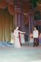 Photograph: [Woman standing on a stage in a dress, gesturing towards a man]