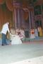 Photograph: [Woman sitting on a stage in a dress, gesturing towards a man]