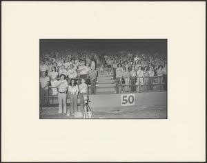 Primary view of object titled '[A crowd of people on bleachers do the Pledge of Allegiance]'.