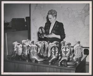 Primary view of object titled '[Enid Justin observing a boot from a table of boots]'.