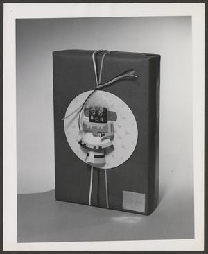 Primary view of object titled '[Product photograph of a Neiman Marcus gift wrapped box embellished with an indigenous doll and string]'.
