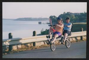 Primary view of object titled '[Two riders on a tandem bike waving: Lone Star Ride 2002 event photo]'.