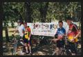 Primary view of [Four cyclists posing by an LSR banner, 2: Lone Star Ride 2003 event photo]