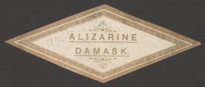 An Alizarine Damask textile label in the shape of a gold diamond with embellishments and outlined patterns. An inscription in pencil is also visible on the top left portion of the label.