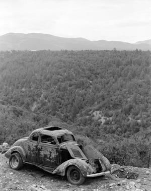 Primary view of object titled '[Abandoned car on a mountain roadside overlooking a forest]'.