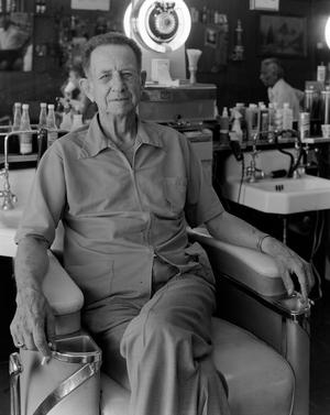 Primary view of object titled '[Jake West sitting in a chair at a barber shop]'.
