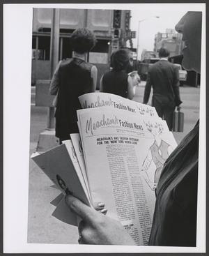 Primary view of object titled '[Photograph of a woman holding a stack of Meacham's Fashion News]'.