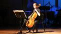 Photograph: [A woman playing a cello in a spotlight onstage]