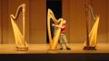 Photograph: [A boy posing with one of three harps on a stage]