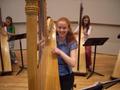Photograph: [A woman in a blue shirt sitting behind a harp]