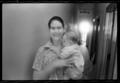 Photograph: [Woman standing in an apartment hallway holding a baby]