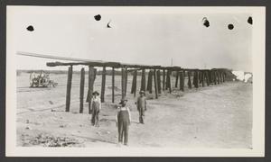 Primary view of object titled '[Three men standing in front of a burned bridge]'.