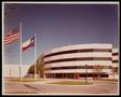 Photograph: [Exterior of an office building with an American flag and Texas flag]
