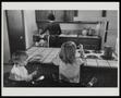 Photograph: [A mother putting away dishes while her kids sit at a counter]